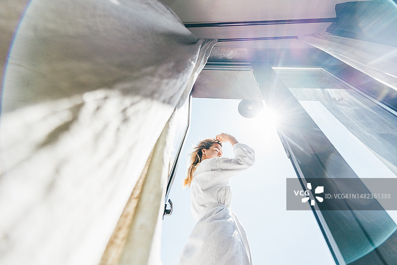 女人在豪华酒店房间里，透过窗户看着打开窗帘图片素材