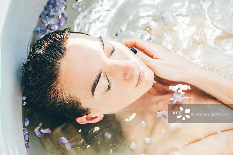 女子在浴缸中放松，漂浮着花瓣图片素材