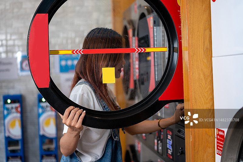 在自助洗衣店里把衣服放进洗衣机的年轻女人图片素材