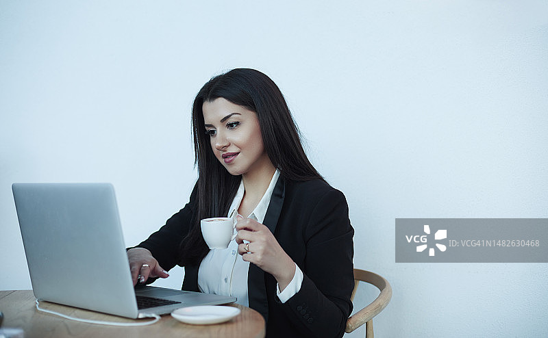 一边喝咖啡一边用笔记本电脑工作的年轻女商人图片素材