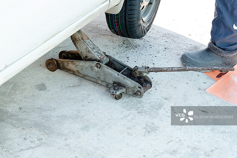 男人用千斤顶抬起汽车更换轮胎特写图片素材