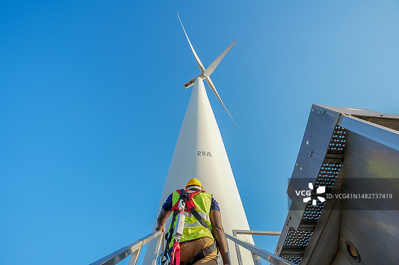 风力发电场技术员站在风力涡轮机杆入口处的背影图片素材