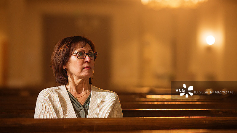 坐在教堂里仔细聆听牧师教诲的年长女人肖像：虔诚的女教区居民在神圣的宗教场所寻找力量和内心的平静图片素材