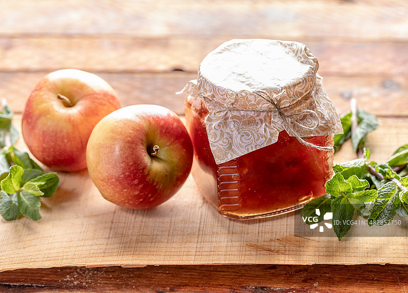 装满苹果酱的小玻璃罐和两个苹果，木制背景上的绿色薄荷，罗马尼亚图片素材