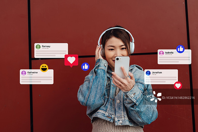 戴耳机用智能手机进行社交媒体的年轻亚洲女性图片素材