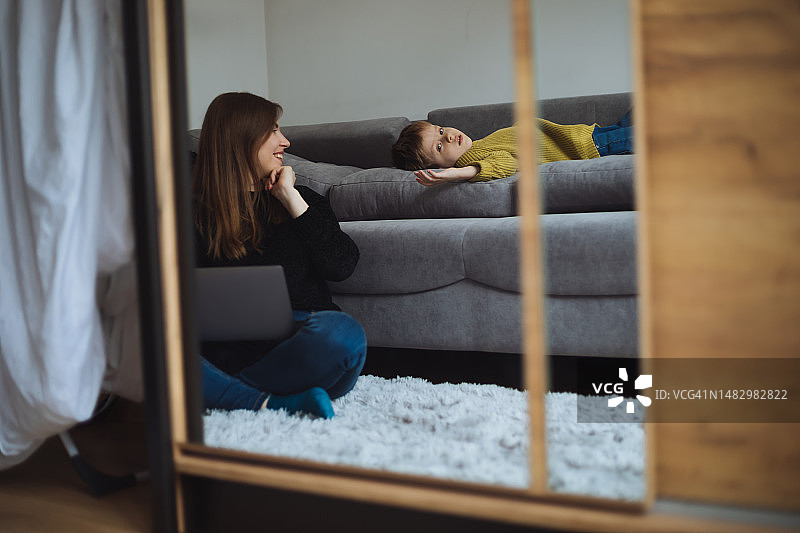 年轻女子和孩子的镜中倒影，居家自由职业者使用笔记本电脑图片素材