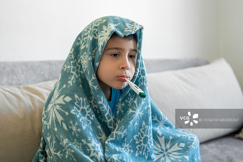 在沙发上用体温计的生病男孩图片素材