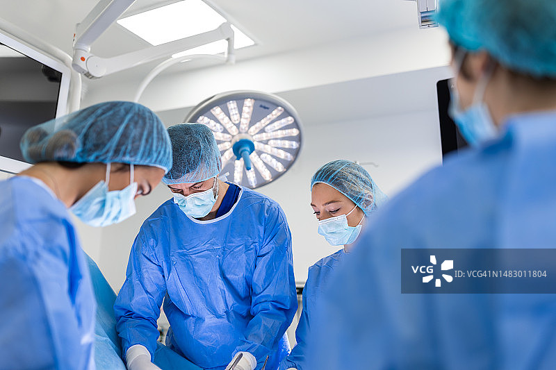 专业外科医生、助手和护士在医院手术室为患者进行侵入性手术。外科医生交谈并使用仪器。真实的现代化医院。图片素材