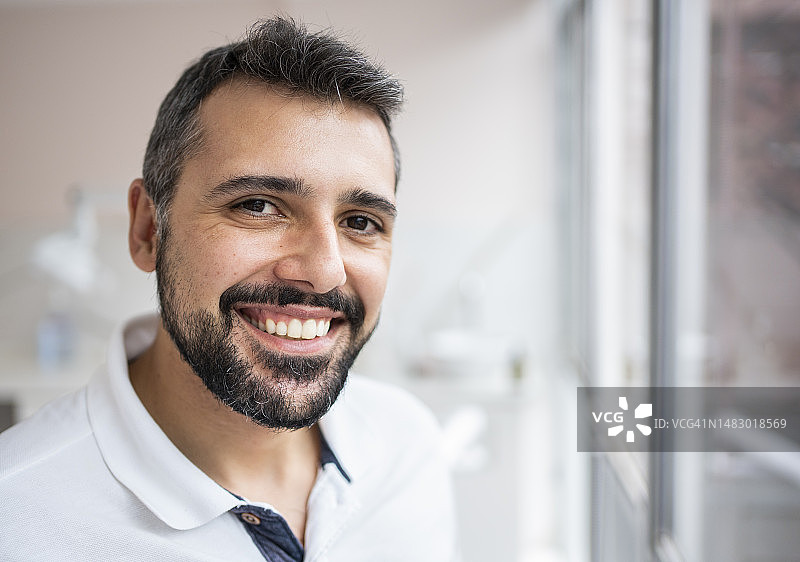 微笑的男牙医站在诊所的窗户旁图片素材
