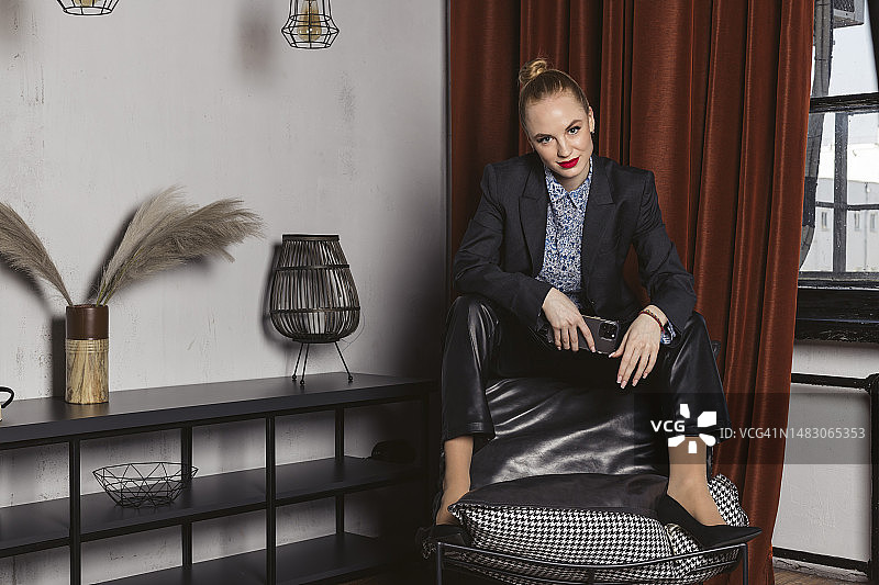 自信的女商人身穿黑色正装，涂着鲜红的口红，在现代办公室或工作室里手持电话摆姿势。图片素材