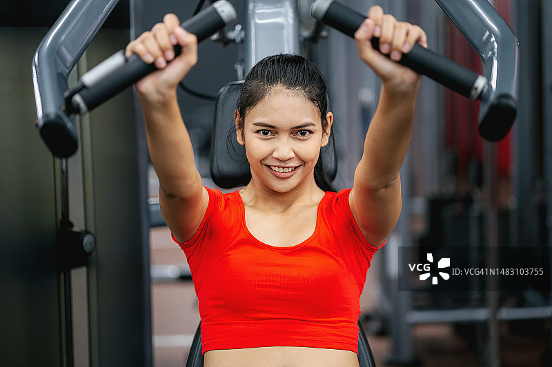年轻女子在健身房使用推举训练器械锻炼，健身概念图片素材