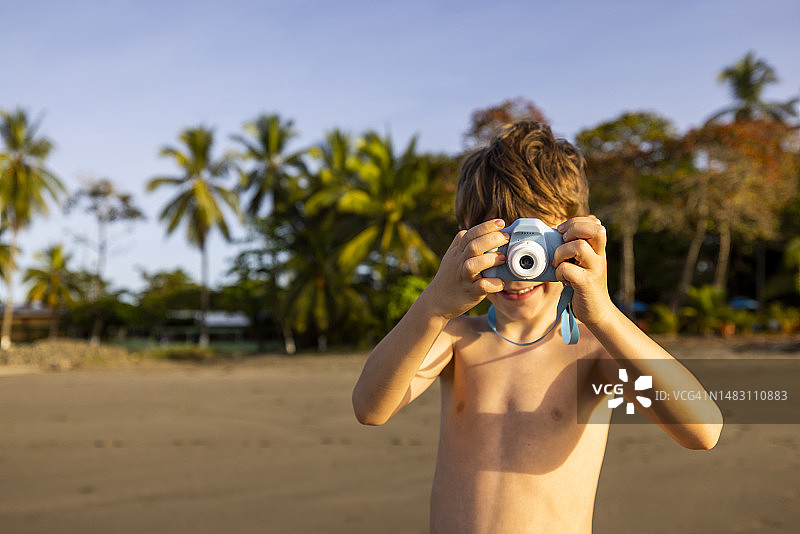 一个在海滩上用小型数码相机拍照的男孩图片素材