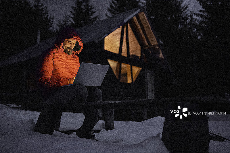 小屋度假：夜晚在小木屋内使用笔记本电脑的男人图片素材