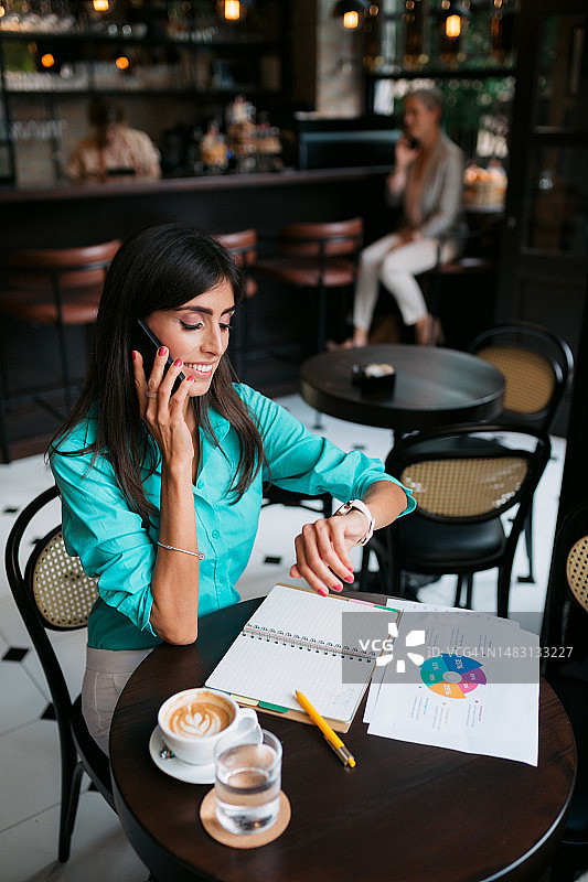 快乐的自由职业女性在咖啡店打电话和查看时间图片素材