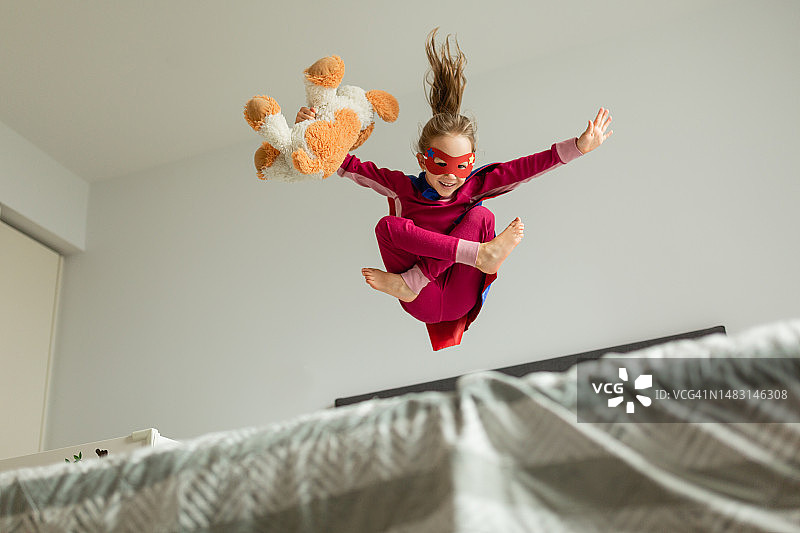 小女孩在家玩超级英雄跳跃游戏图片素材