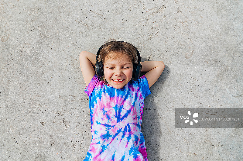 小学生躺在地上，在阳光明媚的日子里戴着耳机图片素材