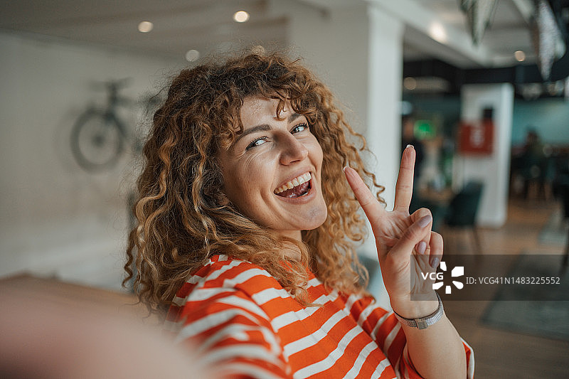 年轻卷发女孩在常去的咖啡馆自拍图片素材