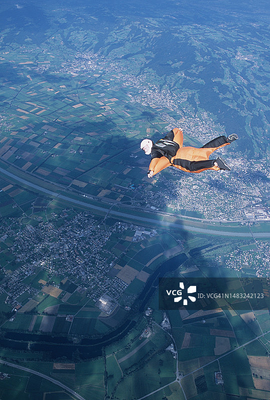 翼装飞行员翱翔于社区和翠绿山谷之上图片素材