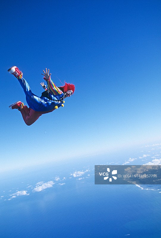 小丑服装跳伞者在云层和海岸线上空自由落体图片素材