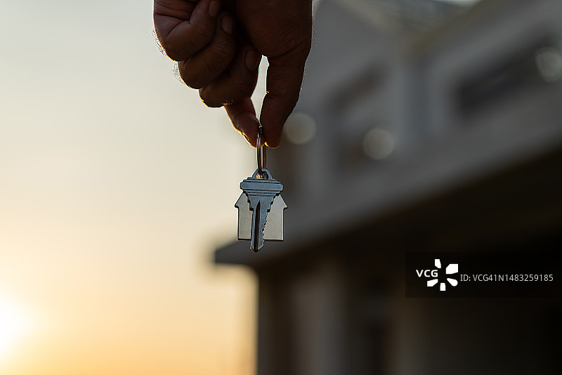 阳光下，男士手持房屋钥匙特写：房地产经纪人在建筑工地，新房购买或租赁，选择购买房产图片素材