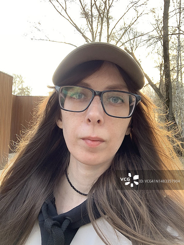 戴眼镜和帽子的年轻女子在公园散步的自拍照图片素材