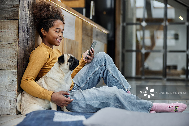 快乐黑人女孩在家和狗狗玩手机图片素材