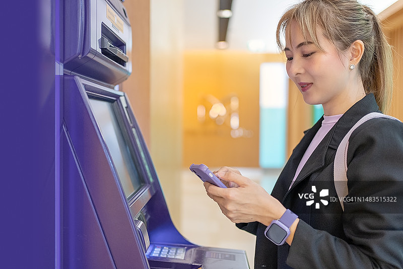 亚洲女商人用智能手机从自动取款机取款图片素材