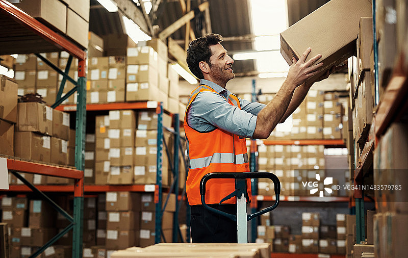 仓库场景：男子从货架上卸下箱子，用于库存或分销。工人搬运箱子，用于物流、存储或运输、货物或供应链的包装图片素材