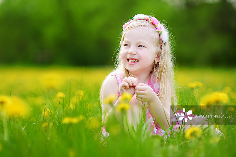 在美丽的春天，可爱的小女孩在盛开的蒲公英草地上图片素材