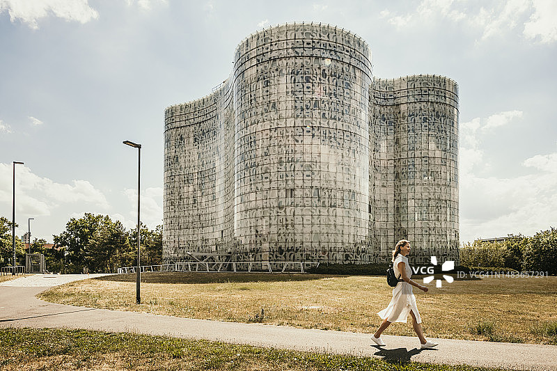 女人在德国科特布斯阳光明媚的图书馆前的人行道上行走图片素材