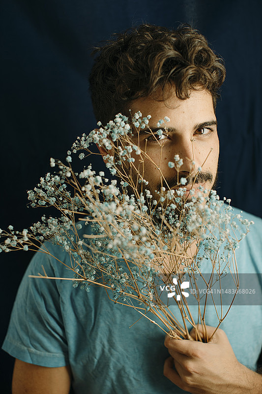 年轻男人拿着鲜花站在蓝色背景前图片素材