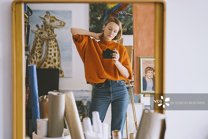 女子在艺术工作室的镜子上拿着相机的倒影图片素材
