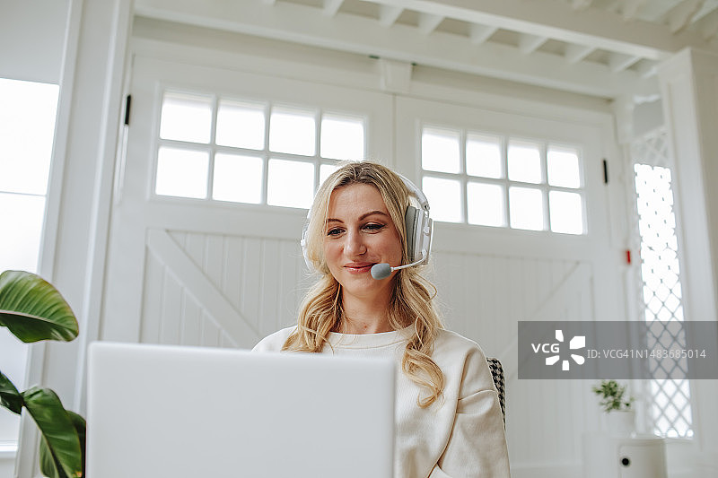 戴着耳机在家用笔记本电脑工作的自由职业者微笑图片素材