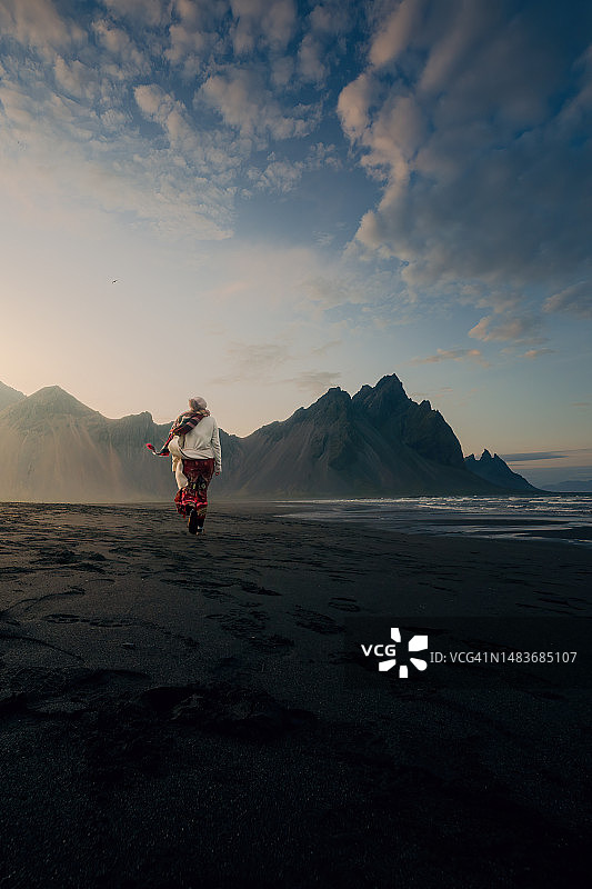 在冰岛斯托克斯内斯海滩日落时分行走的女人，著名地点的风光摄影图片素材