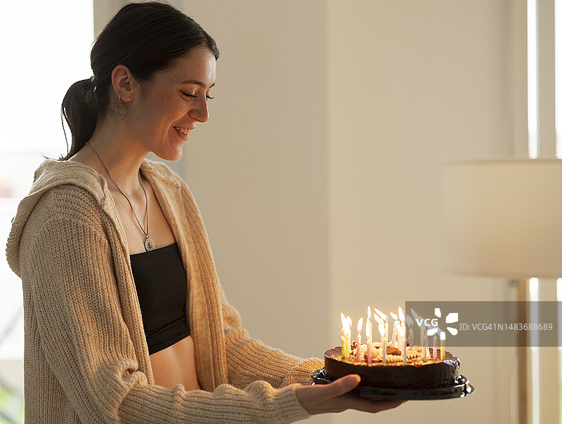 在家拿着生日蛋糕的年轻微笑女人图片素材