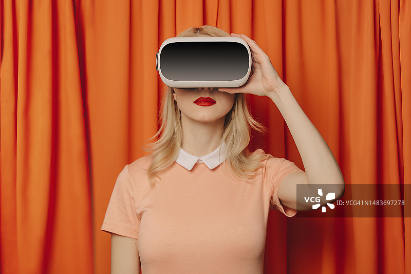 站在橙色窗帘前佩戴VR模拟器的女子图片素材