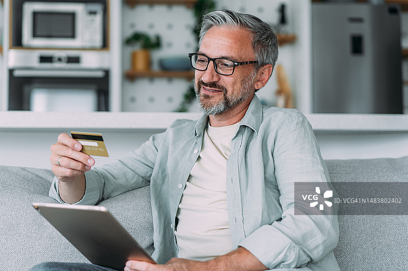 坐在家里的沙发上，用平板电脑在线购物的男人图片素材