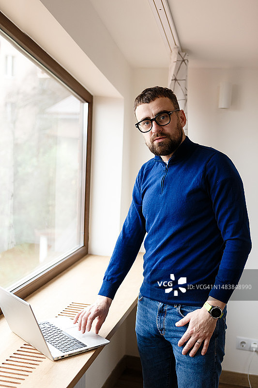 穿着蓝色毛衣和牛仔裤的男人独自在家用笔记本电脑工作图片素材