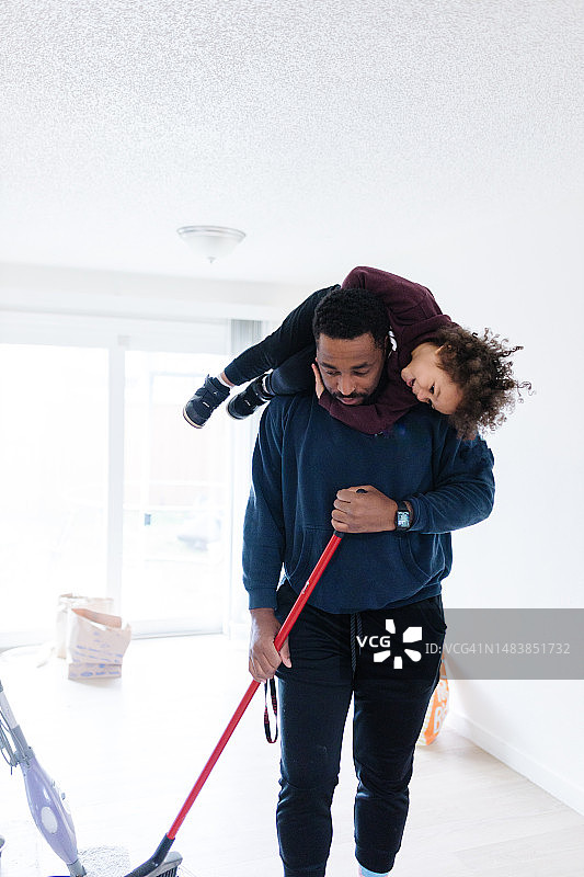 黑人父亲在打扫卫生，扫地，幼儿坐在肩膀上图片素材