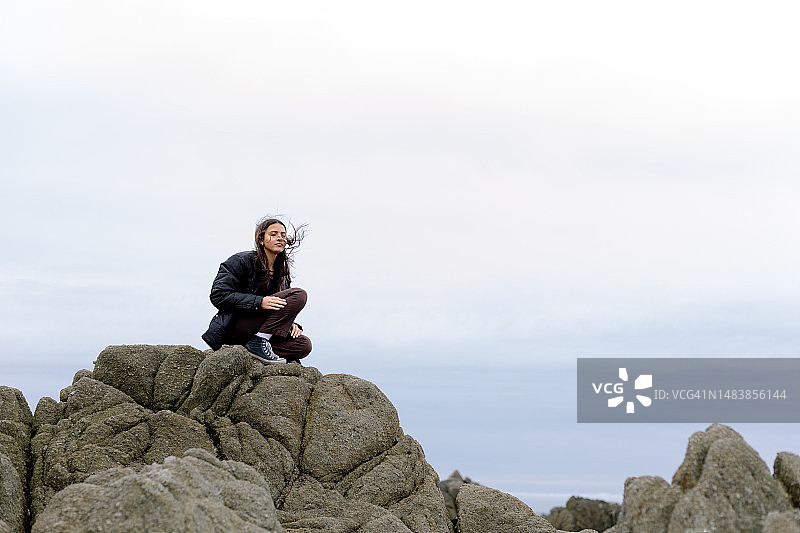 在海滩岩石上被风吹拂的少女图片素材