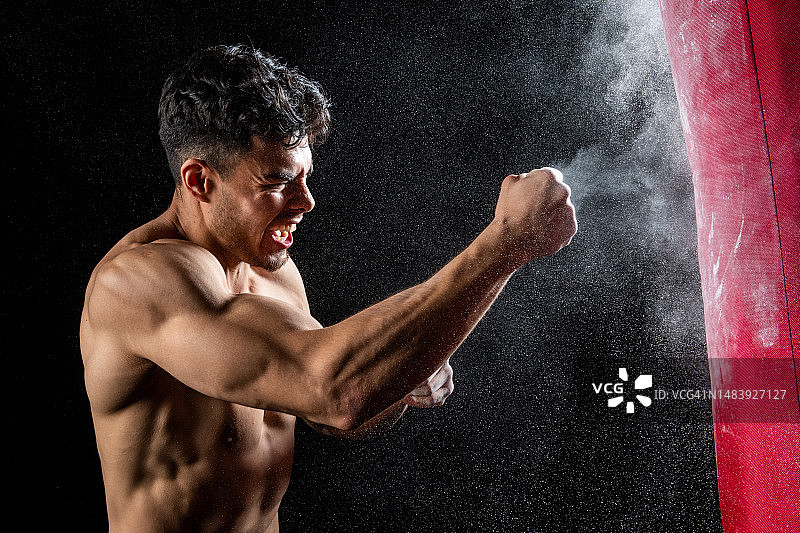 年轻的西班牙裔运动员在黑色背景下击打沙袋图片素材