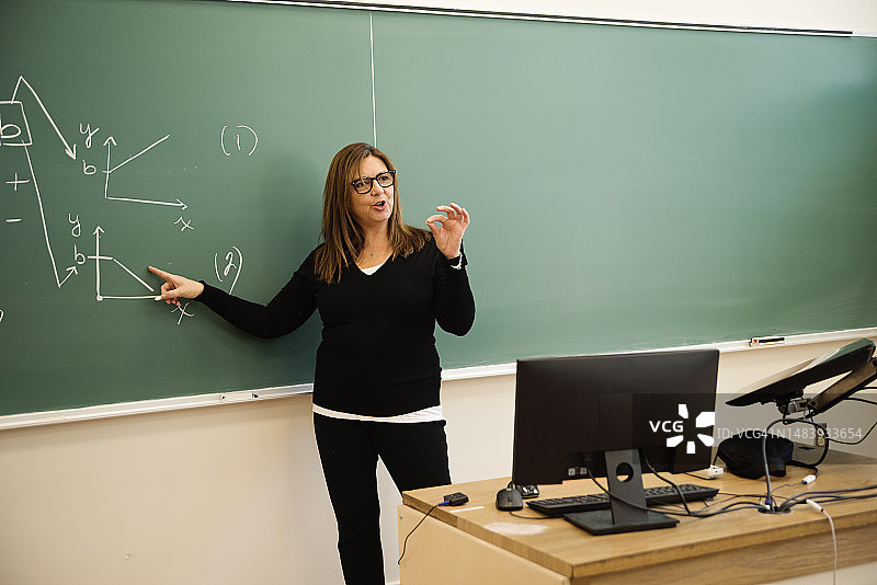 在教室里在黑板上写作的高级女数学老师图片素材