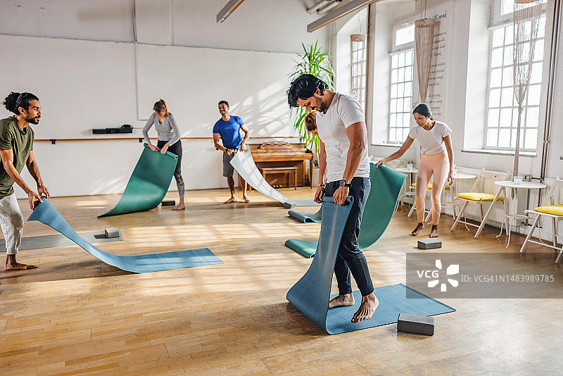 瑜伽课后在舒适温暖的室内折叠瑜伽垫的学员图片素材