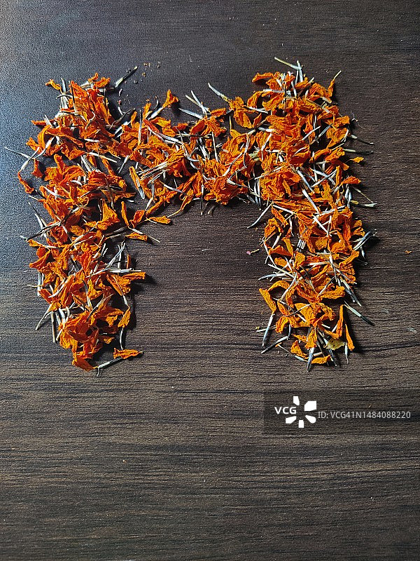 木桌上用干燥万寿菊花/种子拼写的字母“M”图片素材