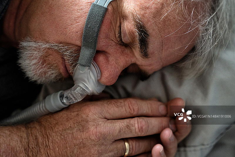 一位60岁男子在床上使用CPAP呼吸机帮助改善呼吸图片素材