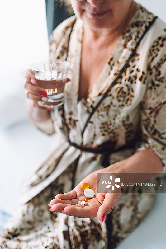 该吃药了：老年女性手拿药丸和水杯图片素材