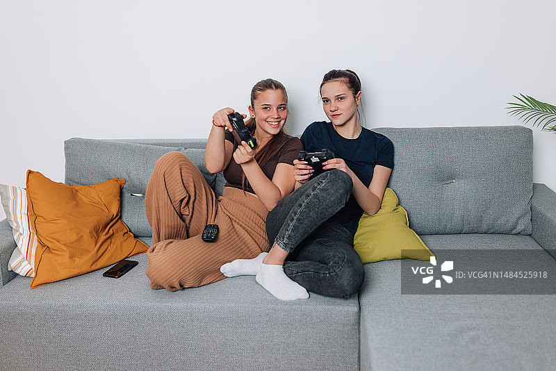 两个少女在沙发上比赛玩电子游戏图片素材