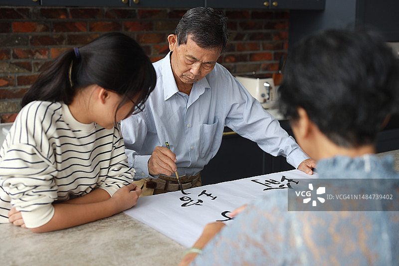 亚洲爷爷在家教妻子和孙女书法，充满温馨和爱图片素材