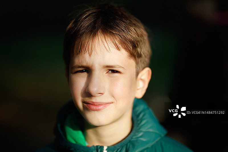 棕色头发和眼睛的青春期前男孩在阳光下皱着眉头看向镜头的头像图片素材