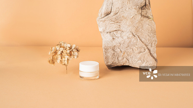 米色背景上带干花的白色化妆品瓶子图片素材